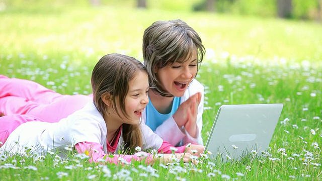 妈妈和女儿在电脑上打字，在公园里大笑。