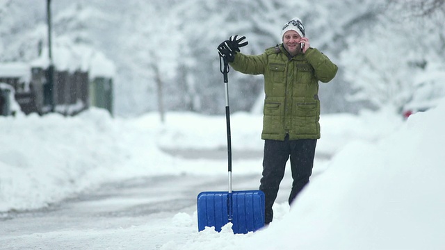 一个男人在铲雪的时候打电话