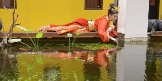 身着红旗袍的女子在池塘边休息