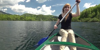年轻女子在山腰的湖中划独木舟