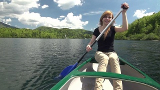 年轻女子在山腰的湖中划独木舟视频素材模板下载