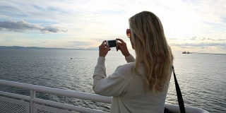 女人从甲板上望向大海，拍照