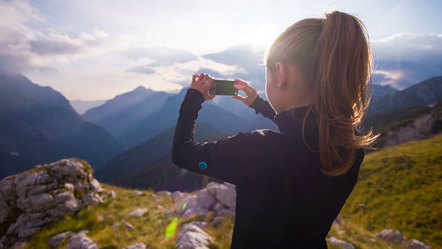 一个女人用智能手机在山坡上拍照