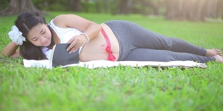 美丽的怀孕亚洲女人放松在公园与红丝带