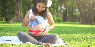美丽的怀孕亚洲女人放松在公园与红丝带