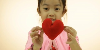 亚洲小女孩展示红色的心枕头
