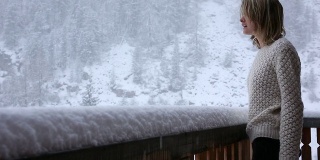 年轻女子走到木屋的阳台上，看着雪花飘落
