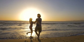 在美丽的海滩上，年轻的夫妇手牵着手，在夕阳下旋转。