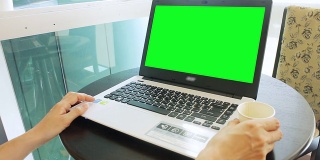 在咖啡馆用绿色屏幕的笔记本电脑工作