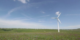 蓝天下旋转的风力涡轮机和草地，实时。