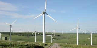 蓝天下旋转的风力涡轮机和草地，实时。