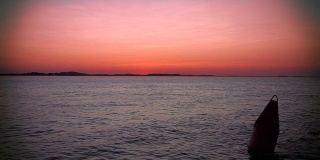 粉红色的夕阳飘过海面，掠过一个浮标