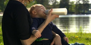 母亲抱着孩子，用奶瓶，奶嘴喝水。
