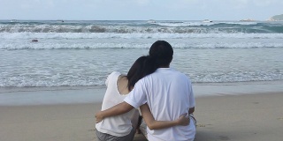 亚洲夫妇互相搂着腰，坐着看海。