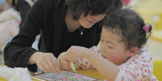 妈妈，亚洲女孩在幼儿园配合涂色画。