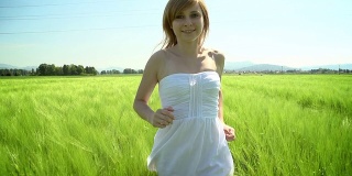 年轻的女人穿着白色的衣服跑过绿色的麦田