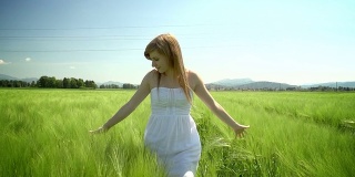 年轻的女人穿着白色的衣服走过绿色的麦田