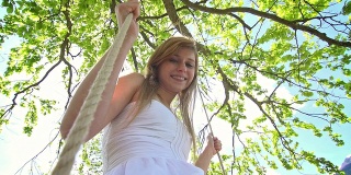 穿白裙子的女孩在树下的绳上荡秋千