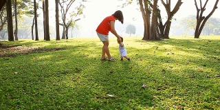 亚洲母亲在公园里帮助婴儿走路。