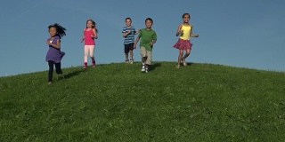 快乐的不同的孩子跑下草坡的慢镜头