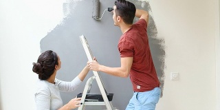 年轻情侣亲吻和油漆墙滚筒