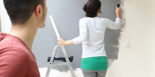 年轻的女人正在用油漆滚筒刷墙