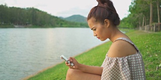 亚洲女性在河边使用智能手机的慢镜头