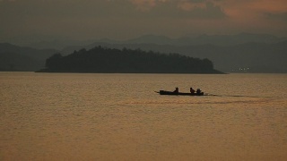 剪影:黄昏时分，渔民们乘坐长船在大坝上回家视频素材模板下载