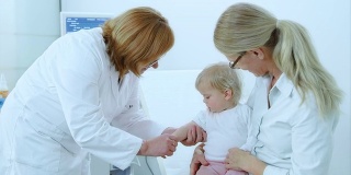 医生给坐在母亲腿上的孩子接种疫苗