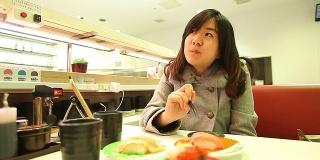 年轻美丽的亚洲女人用筷子吃寿司