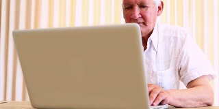 一个老人坐在桌子前用笔记本电脑