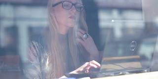 视频剪辑透过一间咖啡馆的窗户，一个女人在用笔记本电脑工作