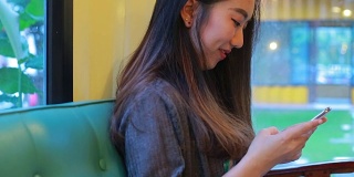 美丽的亚洲女孩在咖啡店打字手机