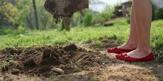 年轻女子穿着红色舞鞋挖花或菜地
