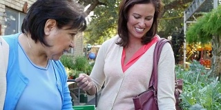 一位成熟的西班牙女性和一位中年白人女性在露天农贸市场谈论绿叶植物