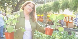 成熟的西班牙妇女试图决定在农贸市场或园艺中心购买哪种绿叶植物