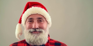 灰色背景上，一位年长的成年人看着镜头，微笑着戴着圣诞老人的帽子。慢动作