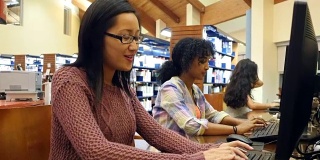 年轻的亚洲女大学生在图书馆的台式电脑上完成作业