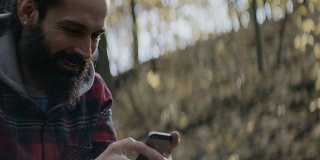 在森林里用智能手机发短信的微笑男人