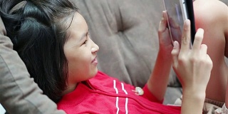 亚洲小女孩在沙发床上玩平板电脑