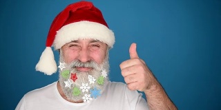 一名成年老人展示了一个拷贝空间，并在蓝色背景上展示了圣诞老人帽子上的拇指