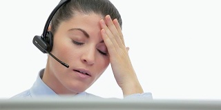 昏昏欲睡的年轻女性客户服务在电脑前通过耳机说话。