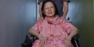 亚洲成年男子照顾他的母亲在轮椅上