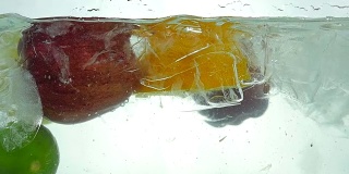 青柠、橙、苹果和柠檬滴在冰水里。关闭了。缓慢的运动。