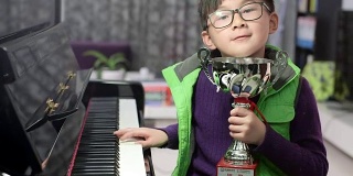 拿着银质奖杯的男孩在钢琴旁