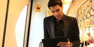 年轻商人在火车上玩平板电脑。