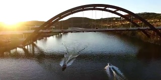 太阳闪光船在水Pennybacker桥或360桥或首都德克萨斯高速公路桥在日落在科罗拉多河或镇湖春天时间空中跟随一艘船在水加速进入阳光