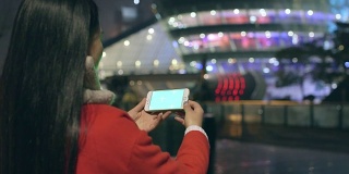 漂亮的亚洲女孩在晚上用智能手机拍照在现代城市