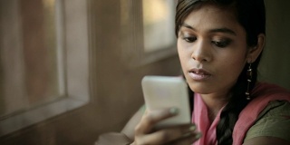 美丽安详的印度女孩坐在窗边读短信。