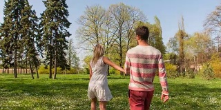 慢镜头:情侣手牵着手穿过公园